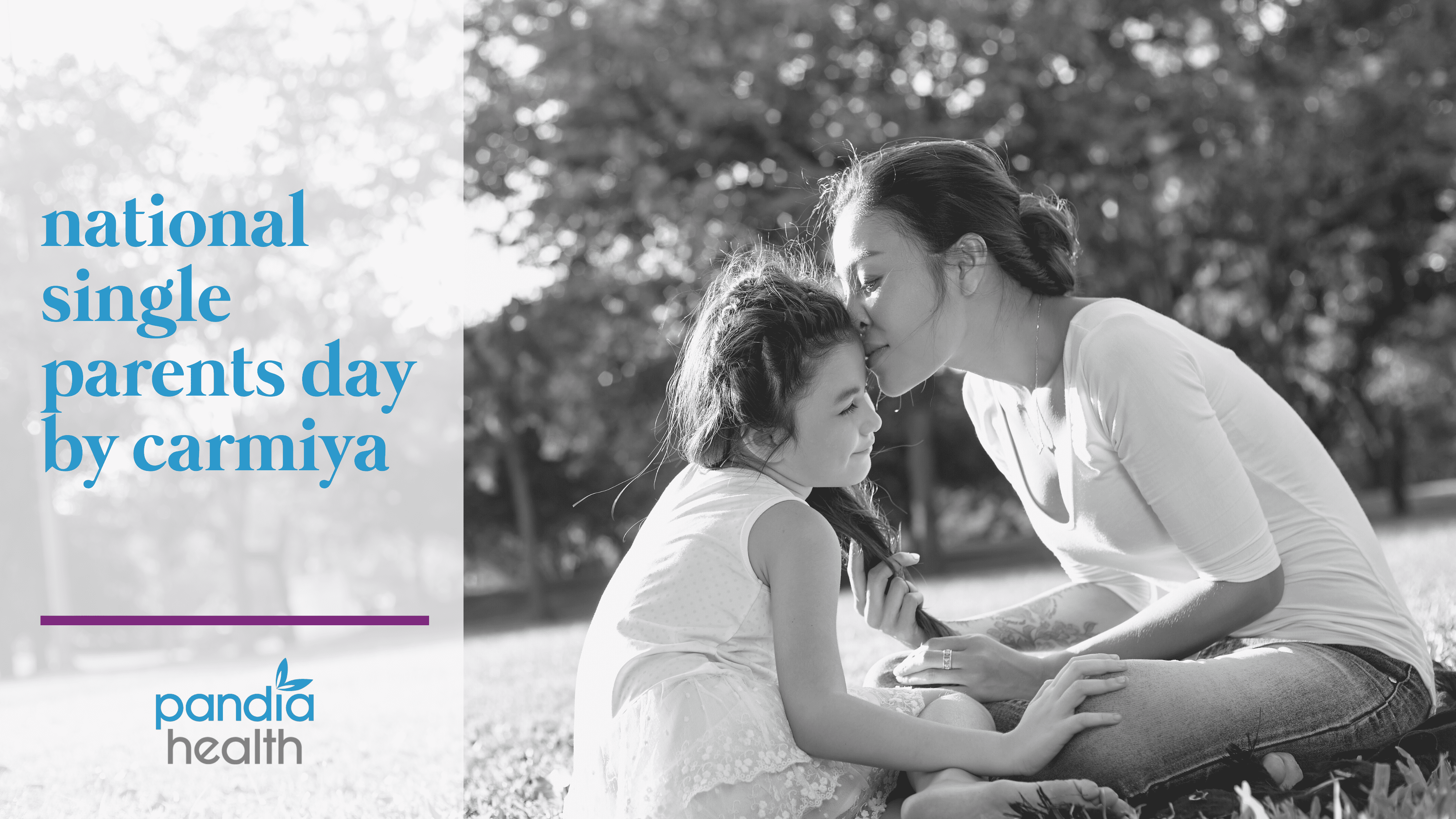 mother and daughter sitting together on the grass as mother kisses her daughter's forehead