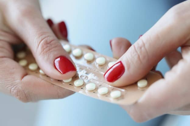 Birth control pills in their packaging held by a woman with red nail polish