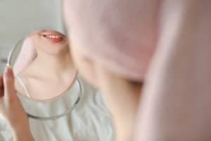 A photo of a woman looking into a handheld mirror and smiling