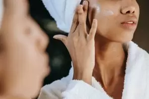 A photo of a woman applying a cream to her cheekbone