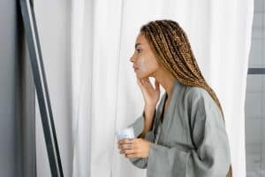 A photo of a woman looking into a mirror and applying a cream to her cheek