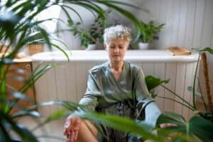 Gray-haired woman meditating in the bathroom at home.