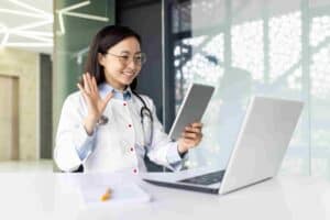Young Asian female doctor working inside medical office consulting patients remotely