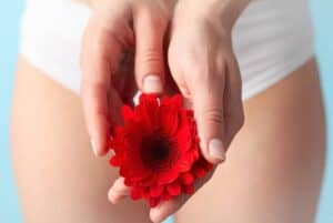 Red flower cupped in hands in front of a background of a a close up shot of a woman wearing underwear