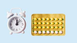 A small clock shown next to a birth control pack against a blue background
