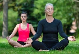 Middle aged woman practicing yoga with younger woman on a green grass lawn