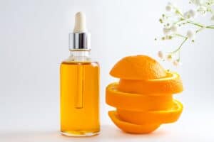 Vitamin C serum in cosmetic bottle with dropper, sliced orange and white flowers on white background 