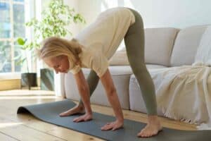 woman in sportswear practicing downward facing dog yoga pose while exercising at home.